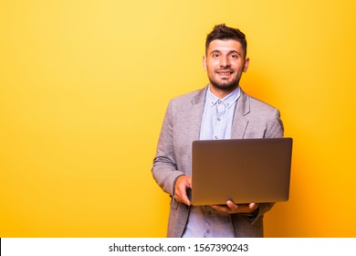 Thoughtful man with a beard dressed in a white T-shirt stands on a yellow background, keeps the laptop in his hands, looks at the screen and thinks.Man with a laptop is isolated on a yellow background - Shutterstock ID 1567390243