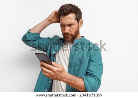 Thoughtful man in casual clothes looking to his mobile phone while standing on white background