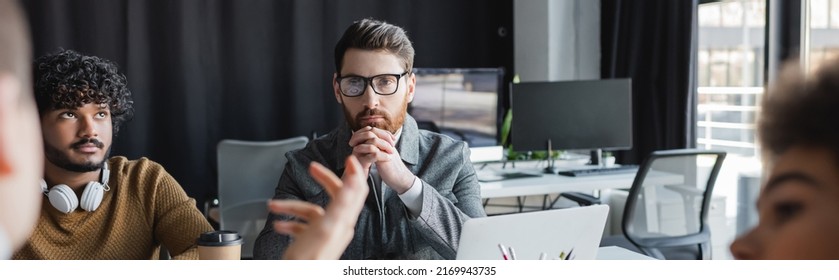 Thoughtful Man In Eyeglasses Near Indian Colleagues And Blurred People In Advertising Agency, Banner