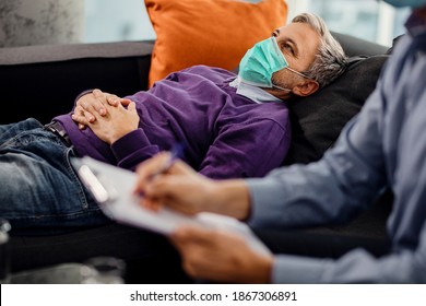 Thoughtful Man With Face Mask Lying Down On Psychiatrist's Couch During A Therapy Session With Mental Health Professional. 