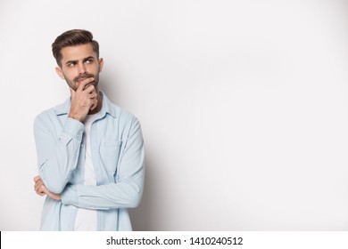 Thoughtful man holding hand on chin pose of indecision, look aside at copy space isolated on white grey studio background considering making difficult feeling doubtful about on freespace text concept - Shutterstock ID 1410240512