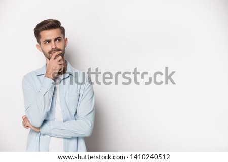 Thoughtful man holding hand on chin pose of indecision, look aside at copy space isolated on white grey studio background considering making difficult feeling doubtful about on freespace text concept