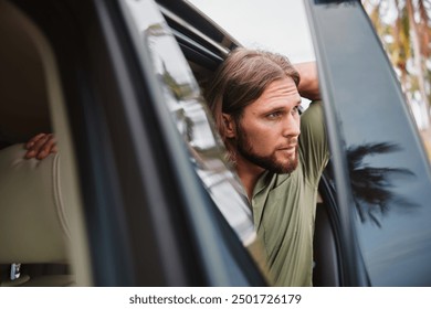 Thoughtful man leaning out of a car window in a serene outdoor setting - Powered by Shutterstock