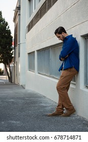 Thoughtful man looking down while leaning on wall