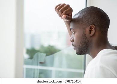Thoughtful man looking out the window in bedroom at home