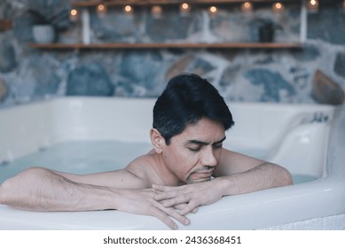 A thoughtful man resting his arms on the edge of a spa hot tub, with a serene expression. - Powered by Shutterstock
