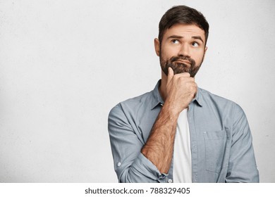 Thoughtful man with stubble looks pensively upwards, has pleasant dreams as plans his coming holidays, generates new ideas, isolated over white background with copy space for your advertising content