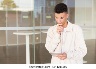Thoughtful man using digital tablet. Portrait of handsome pensive young man standing and using digital tablet near modern building. technology concept