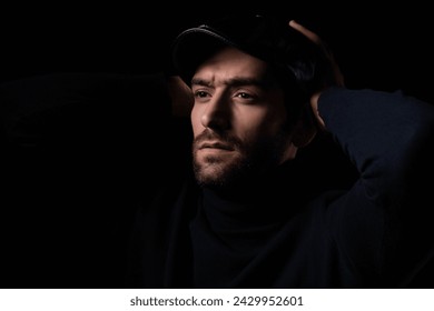 A thoughtful man wearing a black turtleneck and cap, captured in a low-key dramatic lighting setting, evoking introspection.

 - Powered by Shutterstock