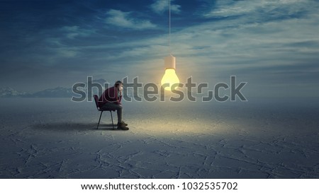 Thoughtful man in wilderness looks to a yellow light bulb coming down from the sky.