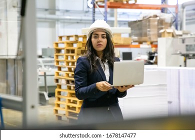 Thoughtful Manager Holding Laptop At Printing Factory. Focused Asian Employee Holding Open Laptop At Manufacturing Plant. Print Manufacturing Concept