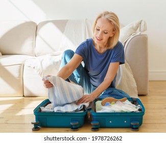 Thoughtful mature 60s woman packing suitcase, preparing luggage for travel trip while sitting on wooden floor at home. Senior lady getting ready for summer vacation. Traveling in retirement concept - Powered by Shutterstock