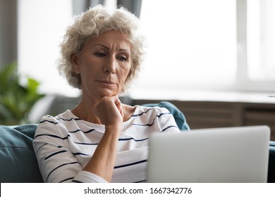 Thoughtful Mature 60s Woman Sit Rest On Couch Watch Video Or Movie On Laptop, Pensive Middle-aged 50s Grandmother Relax In Living Room At Home Use Computer Enjoying Leisure Weekend Indoors