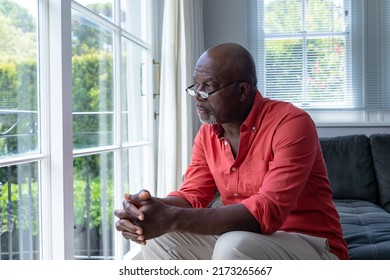 Thoughtful mature african american man looking though window while sitting at home, copy space. Unaltered, contemplation, people, lifestyle and home concept.