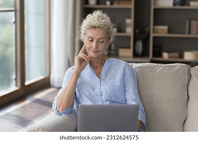 Thoughtful mature freelancer woman working at laptop at home, resting on soda, holding computer, watching, reading content, touching chin, thinking, using Internet technology for freelance job - Powered by Shutterstock