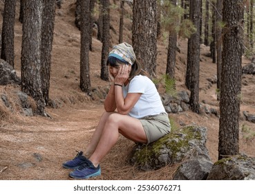 Thoughtful mature woman with face in hands sitting outdoors during a hike in the woods - Powered by Shutterstock