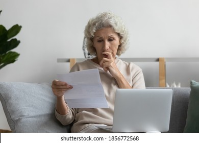 Thoughtful Mature Woman Reading Letter, Touching Chin, Using Laptop, Working With Correspondence, Sitting On Couch At Home, Pensive Serious Middle Aged Female Holding Documents, Making Decision