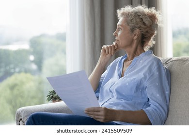 Thoughtful mature woman sitting on sofa at home, hold papers looking away, think of financial problems, make decision, analyze payment notification, feel doubt, get unpleasant message in postal letter - Powered by Shutterstock