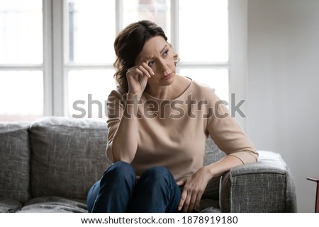 Thoughtful mature woman touching forehead, lost in thoughts, memories, sitting on couch at home alone, upset pensive middle aged female looking in distance, thinking about problems, pondering 商業照片 © 