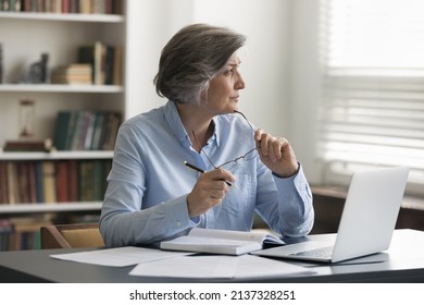 Thoughtful middle-aged businesswoman takes off glasses staring out window, solve issue, search ideas, develop business strategy, sit at workplace desk with laptop, pensive employee pondering in office - Powered by Shutterstock