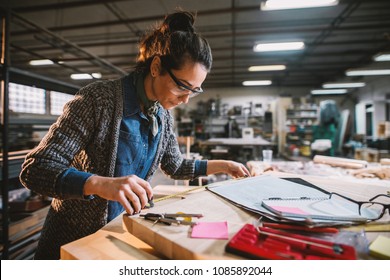 Thoughtful middle-aged industrial female engineer with eyeglasses working with a tape measure in the workshop. - Powered by Shutterstock