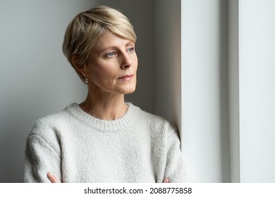 A thoughtful middle-aged woman looks out the window and is sad - Powered by Shutterstock