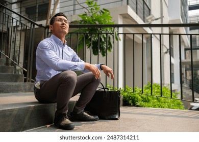 Thoughtful millennial businessman sitting on stairs with briefcase looking away. - Powered by Shutterstock