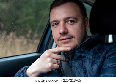 Thoughtful millennial man rides in car in passenger seat in rainy weather