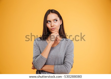 Thoughtful model in studio looking away. hand near the face. isolated orang background