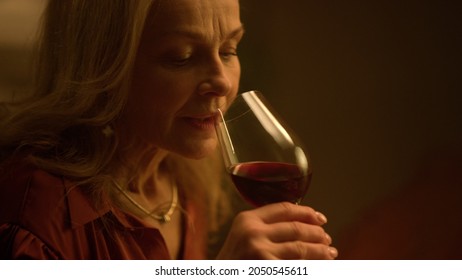 Thoughtful old aged woman drinking red wine glass at restaurant date. Closeup melancholy mature lady tasting alcohol drink indoors. Sad grandmother wife thinking about upset retirement life concept