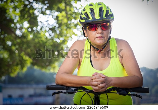 Thoughtful old woman in protective\
sportswear leaning on bicycle handlebar with water\
bottle