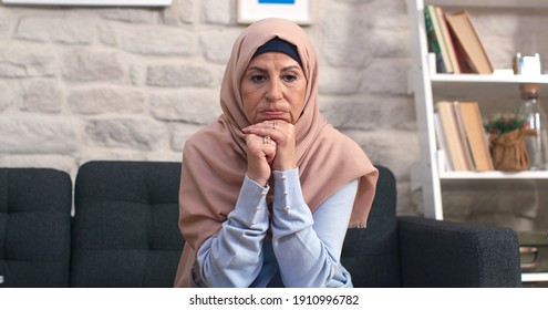 The thoughtful old woman in a turban sits alone on the sofa, thinking about the problem of loneliness Pensive sad old woman in turban feels anxious depression at home due to anxiety and loneliness.