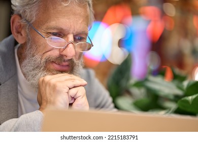 Thoughtful Older Senior Business Man Office Executive Wearing Glasses Looking At Laptop. Mature Old Professional Businessman Teacher Wearing Suit Working Late On Computer Watching Webinar Online.