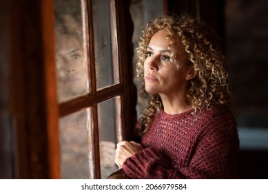 Thoughtful portrait of attractive adult woman at home looking outside the windows reflected on the gass. Worried adult female people alone indoor. Depression sadness concept