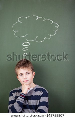 Thoughtful preadolescent student standing against chalkboard with thought bubble drawn on it