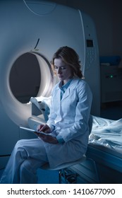 Thoughtful Radiologist Using Digital Tablet While Sitting Near Computed Tomography Scanner 