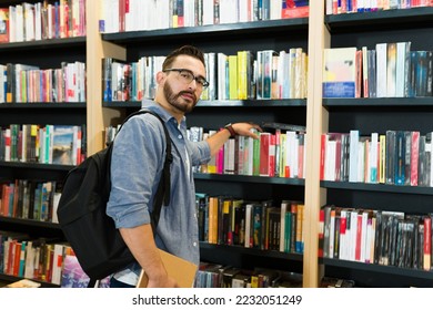 Thoughtful reader man with a backpack looking for a novel on the bookshelves of the bookstore
