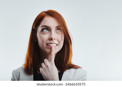 Thoughtful redhead with an inquisitive expression, gently touching her chin, dressed in a sophisticated white blazer