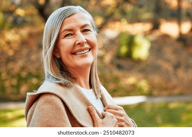 A thoughtful and reflective senior woman takes pleasure in a serene moment within a picturesque autumn park, where she is surrounded by an array of vibrant, colorful leaves that enhance the scene - Powered by Shutterstock