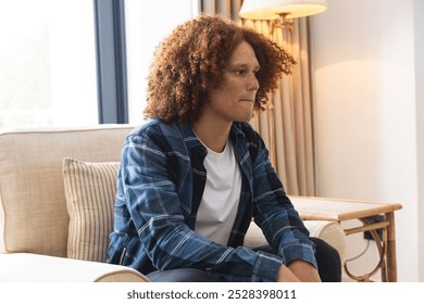 Thoughtful, sad biracial man sitting in armchair in living room at home. Depression, mental health, lifestyle and domestic life, unaltered. - Powered by Shutterstock