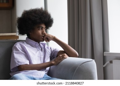 Thoughtful Sad Teen Black Guy With Retro Afro Hairstyle Sitting On Sofa At Home, Looking Away, Thinking, Feeling Anxious, Bored, Concerned, Suffering From Depression. Youth Problems Concept