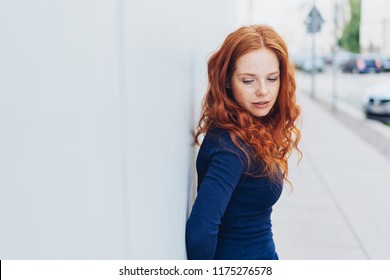 Thoughtful sad young woman with downcast eyes leaning against a white exterior wall in a town street with copy space - Powered by Shutterstock