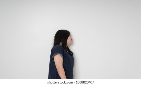 Thoughtful sad young woman with downcast eyes leaning against a white exterior wall  with copy space