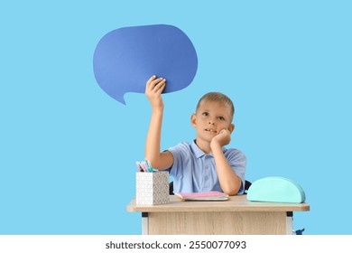 Thoughtful schoolboy with stationery and blank speech bubble sitting on desk against blue background - Powered by Shutterstock