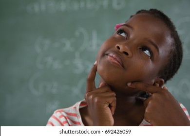 Thoughtful schoolgirl sitting against chalkboard
