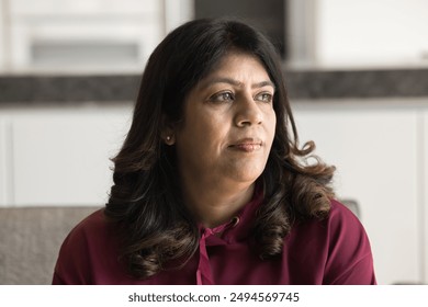 Thoughtful senior Indian woman in casual sitting on home couch, looking away in deep thoughts, thinking on aging health problems, feeling lonely, depressed. Pensive mature female model casual portrait - Powered by Shutterstock