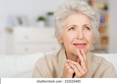 Thoughtful senior lady sitting at home with her fingers to her chin reminiscing and recalling fond memories, close up portrait
