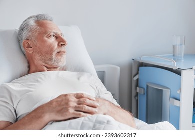 Thoughtful senior male patient in hospital bed in ward room. Treatment and healing. Recuperation after illness disease. Depression - Powered by Shutterstock