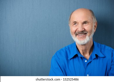 Thoughtful senior man daydreaming looking up into the air with a smile as he stands against a blank green chalkboard with copyspace - Powered by Shutterstock