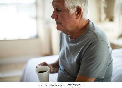 Thoughtful senior man holding mug of black coffee in the bedroom at home